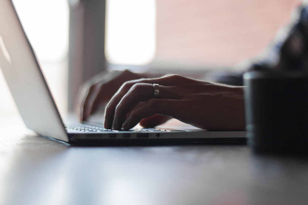 Typing at a desk with a notebook open beside a keyboard.